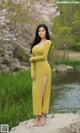 A woman in a yellow dress standing on a rock by a river.