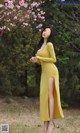 A woman in a yellow dress standing in front of a flowering tree.