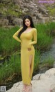 A woman in a yellow dress standing on a rock by a river.