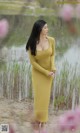 A woman in a long yellow dress standing by a lake.