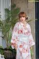 a woman in a white kimono standing next to a plant