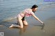 A woman in a pink bikini crouching down on the beach.