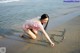 A woman in a pink bikini writing in the sand on the beach.