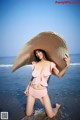 A woman in a pink bikini and a straw hat on the beach.