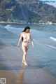 A woman in a pink bikini walking on the beach.