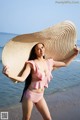 A woman in a pink bikini and a straw hat on the beach.