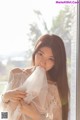 A woman in a white dress is posing by a window.