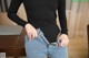 A woman in a black bodysuit is holding a pair of jeans.