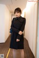 a woman in a black trench coat standing in a hallway