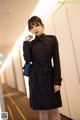 a woman wearing a black trench coat standing in a hallway