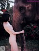 A naked woman standing next to an elephant in a field.