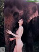 A naked woman standing next to an elephant.