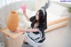 A woman in a maid outfit cleaning a bed with a pink duster.