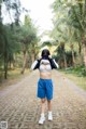 A woman in a sports bra top and blue shorts standing on a dirt road.