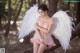 A woman in a pink dress with white wings sitting on a tree branch.