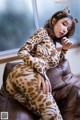 A woman in a leopard print catsuit sitting on a brown couch.