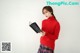 a woman in a red sweater and plaid skirt holding a book