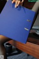 A woman sitting at a desk holding a blue folder.