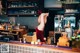 A woman in a red dress standing behind a bar.