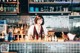 A woman behind a bar with bottles of alcohol behind her.