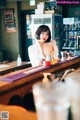 A woman sitting at a bar in a white shirt.