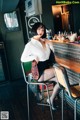 A woman sitting at a bar in a white shirt and black skirt.