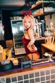 A woman in a red dress standing behind a bar.