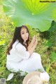 A woman in a white dress sitting in the grass holding an umbrella.